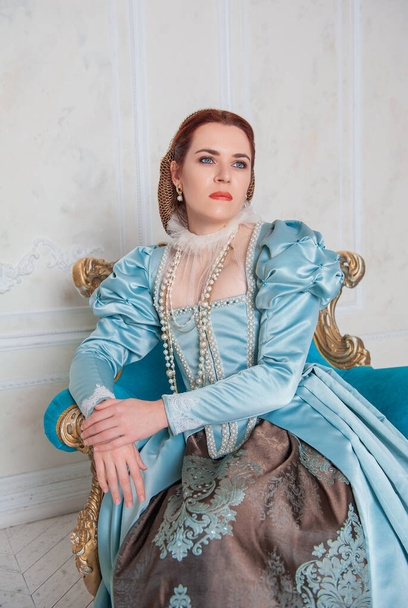 Hermosa mujer joven de estilo medieval vestido azul sentado en el armchai - Foto, Imagen