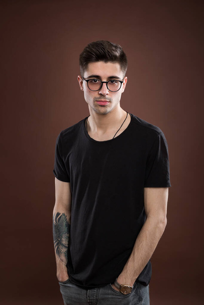 Young man in depression. Stylish male student wears round spectacles, has trendy hairstyle, looks confidently, isolated over brown background. People and human expressions. - Fotó, kép