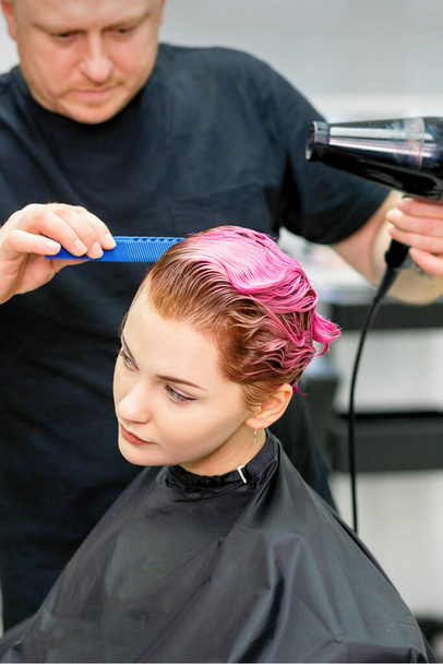Una peluquera está secando el pelo rosa de la joven en un salón de belleza - Foto, Imagen