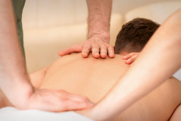 Młody mężczyzna otrzymuje masaż pleców w czterech rękach w salonie piękności spa - Zdjęcie, obraz