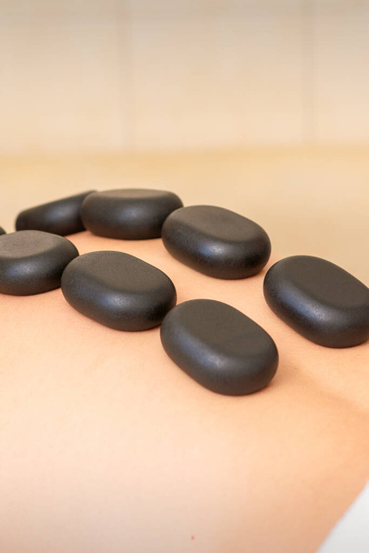 Hot stone massage therapy. Caucasian young man getting a hot stone massage on back at spa salon - 写真・画像