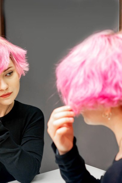 Gyönyörű fiatal kaukázusi nő nézi a rövid rózsaszín haj a tükörben - Fotó, kép