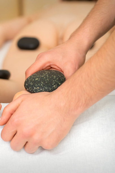 Twee masseurs maken een voetmassage met een hete steen in vier handen in de spa - Foto, afbeelding