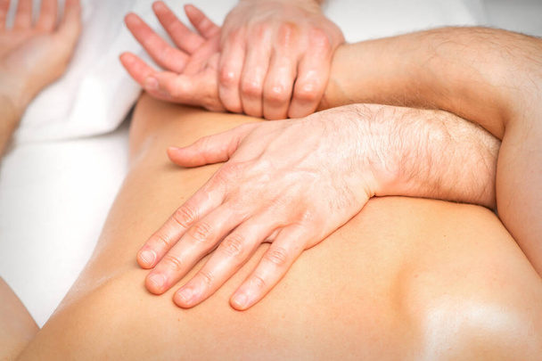 Un physiothérapeute masculin étire les bras sur le dos d'un homme allongé, ferme - Photo, image