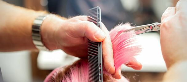 Femme ayant une nouvelle coupe de cheveux. Homme coiffeur coupe les cheveux roses avec des ciseaux dans un salon de coiffure, gros plan - Photo, image