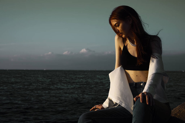 Портрет молодої мрійливої жінки на камені біля моря. розслаблююча дівчина відпочиває на узбережжі, насолоджуючись відпочинком на відкритому повітрі
. - Фото, зображення
