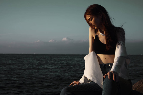 Porträt einer jungen träumenden Frau auf Steinen am Meer. entspannendes Mädchen ruht sich an der Küste aus und genießt die Erholung im Freien. - Foto, Bild