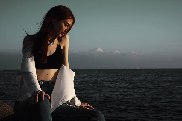 Портрет молодой мечтательницы на камнях у моря. расслабляющая девушка отдыхает на побережье, наслаждаясь отдыхом на открытом воздухе. - Фото, изображение