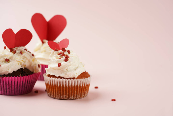 Trois muffins faits maison au chocolat et blanc avec glaçage crémeux blanc et décoration de sucre rouge et blanc partagée par le cœur sur du marbre sur une surface rose - Photo, image