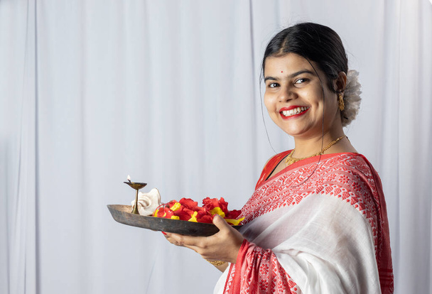 Красива індійська жінка в червоному сарі тримає пуджа талі або молитовний стовп на білому тлі. - Фото, зображення