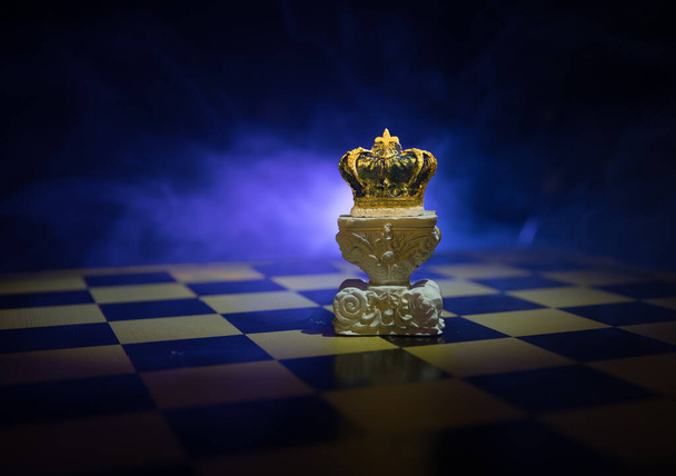 Hermosa corona en el tablero de ajedrez. ajedrez concepto de juego de mesa de ideas de negocios y competencia y concepto de ideas de estrategia. Figuras de ajedrez sobre un fondo oscuro con humo y niebla. Enfoque selectivo - Foto, imagen