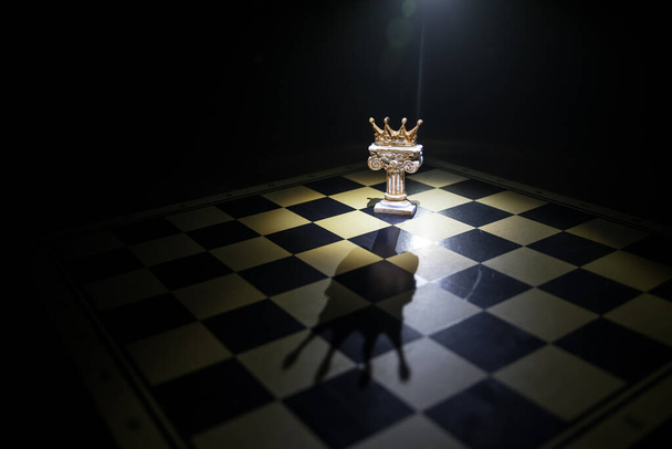 Bonita miniatura coroa no tabuleiro de xadrez. conceito de jogo de tabuleiro de xadrez de ideias de negócios e competição e conceito de ideias de estratégia. Figuras de xadrez em um fundo escuro com fumaça e nevoeiro. Foco seletivo - Foto, Imagem