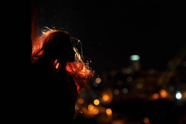Sylwetka kobiecej twarzy na jasnym tle. SIlhouette samotnej lalki z długimi włosami w nocy ze światłami miejskimi na tle. Skupienie selektywne - Zdjęcie, obraz