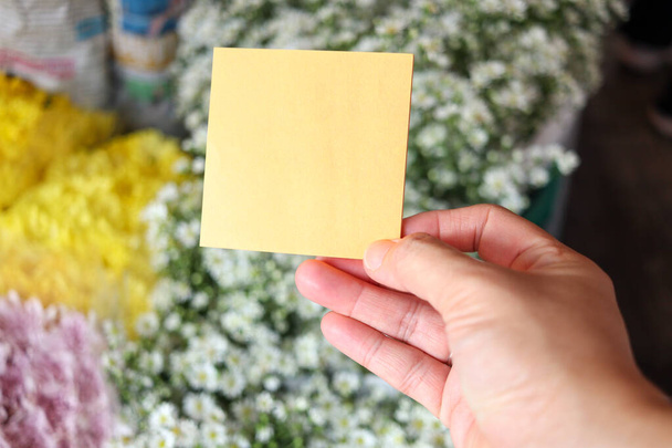 Blanco notitie papier in de hand op mooie witte snijder bloem boeket achtergrond, kopieer-ruimte op de kaart om uw bericht. - Foto, afbeelding