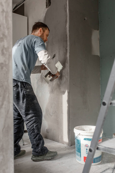 Человек-мастер европейского вида штукатурирует стены, проводит ремонт в квартире, концепцию ремонта и реконструкции дома - Фото, изображение