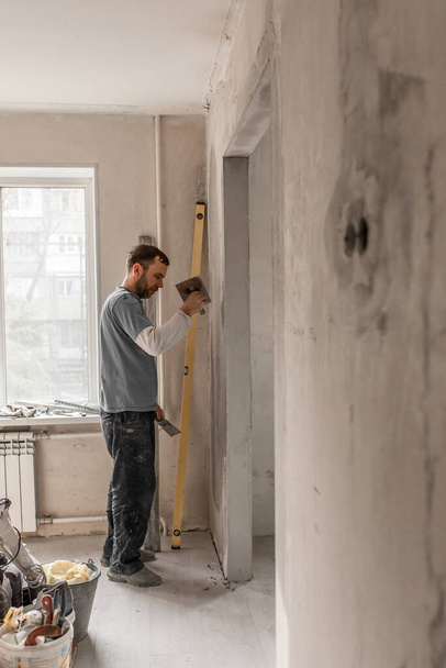 Un hombre-un maestro de la apariencia europea escayola las paredes, hace reparaciones en el apartamento, el concepto de reparar y remodelar la casa - Foto, imagen