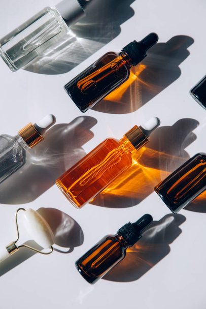 Um conjunto de muitas garrafas de vidro diferentes com líquidos cosméticos dispostos em uma fileira. O jogo de luz cria padrões abstratos de sombras.  - Foto, Imagem