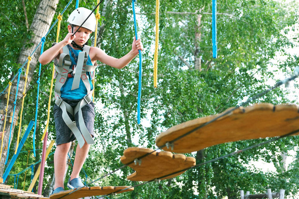 Junge beim Sommervergnügen im Abenteuerpark an der Seilrutsche. Balancierbalken und Seilbrücken - Foto, Bild