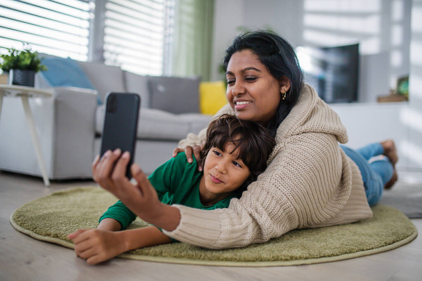 Indian mother lying on floor with her little son at home, taking selfie. - Zdjęcie, obraz