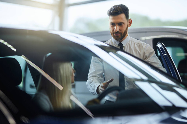Salesman showing to female customer new car at showroom - Фото, изображение