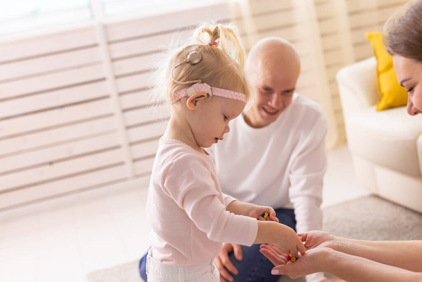 Ребенок с кохлеарными имплантами играет с игрушками дома. Концепция глухоты и медицинских технологий. - Фото, изображение