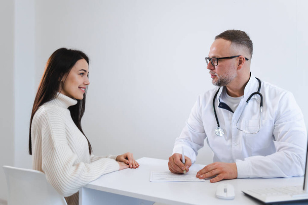 Male doctor writing a prescription for her patient. Physician consulting a young woman - Photo, Image