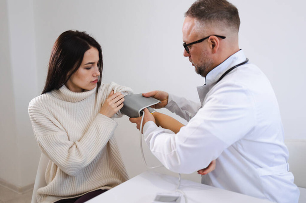 Mieslääkäri laittaa naispotilaan käsivarteen verenpainemittarin rannekkeen - Valokuva, kuva