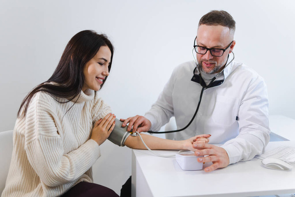 Médico do sexo masculino no exame médico mede a pressão arterial de uma paciente mulher. Mulher na consulta no cardiologista - Foto, Imagem