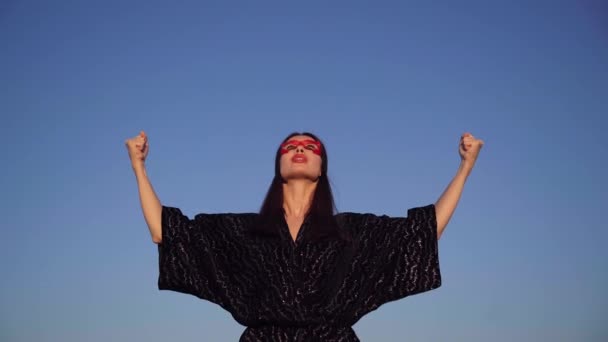 Υπερηρωίδα γυναίκα με μάσκα κοιτάζει ψηλά με τα χέρια απλωμένα - Πλάνα, βίντεο