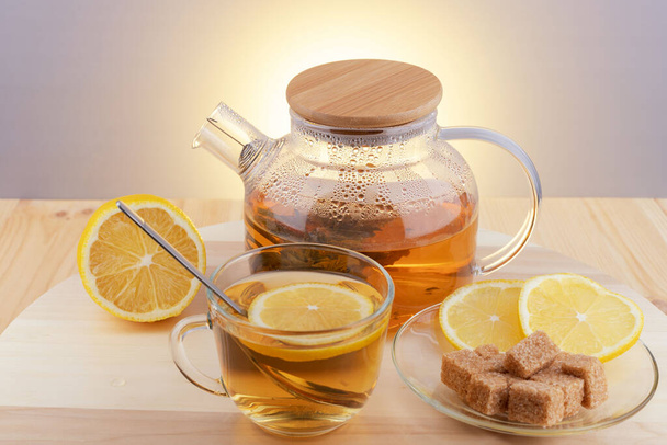 グラスティーポットやスプーン付きのグラスカップでお茶,木製のテーブルの上にレモンスライスと黒糖. - 写真・画像