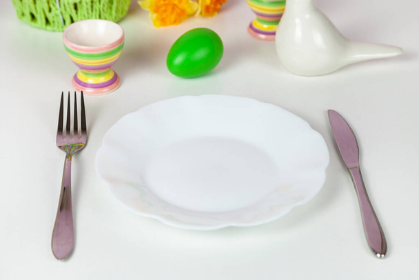 Easter table setting and dinner with yellow flowers, festive decorations, white bird and multicolored eggs. Close up. - Foto, afbeelding