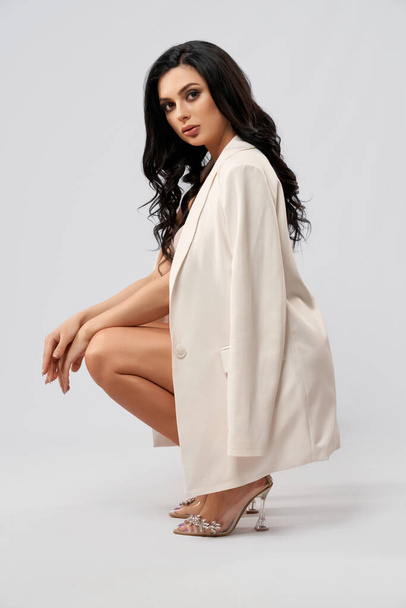 Lady in stylish white jacket and high heels posing in studio - Foto, afbeelding
