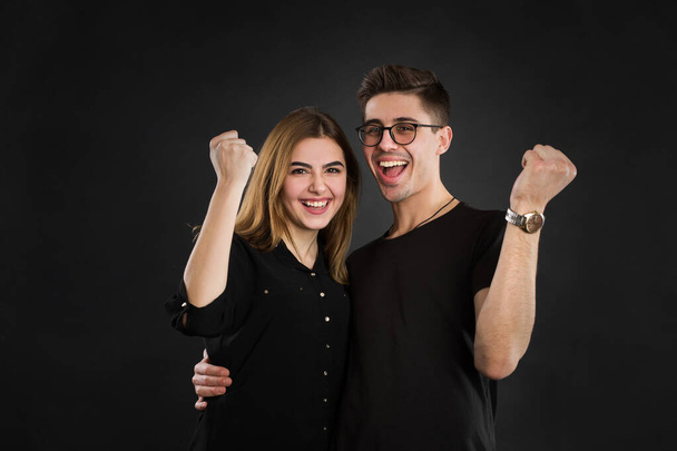 Yes We did it Cheerful couple is celebrating with raised hands, standing on black background in shirt People, happiness, winning, victory, success and good luck - Foto, Imagem