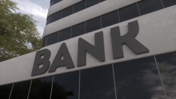 Bank sign on a modern glass skyscraper. Mirrored sky and city on modern facade. Business and finance concept - Footage, Video