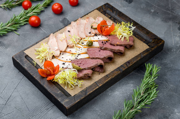 slicing of different meat on the board on grey table - Фото, изображение