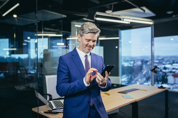 Business manager, businessman in a modern office, uses the phone, happy and happy, experienced man - Fotoğraf, Görsel
