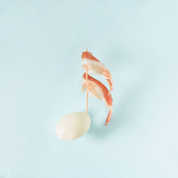 Μπέικον με αποφλοιωμένο αυγό σε παστέλ μπλε φόντο. Ελάχιστη έννοια τροφής. Creativ ιδέα διακοπών. - Φωτογραφία, εικόνα