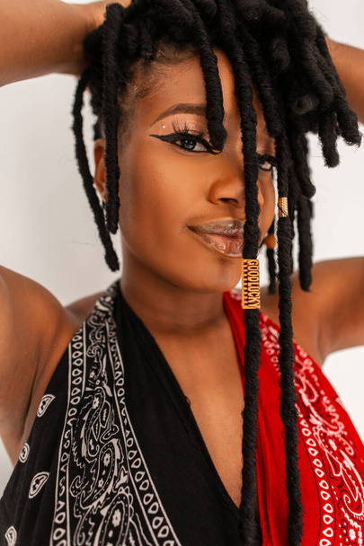 Retrato joven mujer africana modelo en moda rojo-negro sexy botín superior endereza rastas peinado sobre fondo blanco. Ricitos cubren la cara afro chica. Close-up belleza femenina cara negra. - Foto, Imagen