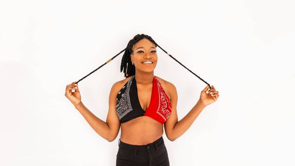 Pozitív fiatal afrikai nő vidám mosollyal, trendi piros-fekete kendős toppal, fehér háttérrel a stúdióban. Aranyos mosolygós afro-amerikai lány modell, szajré ruhákat visel. Modern divat. - Fotó, kép