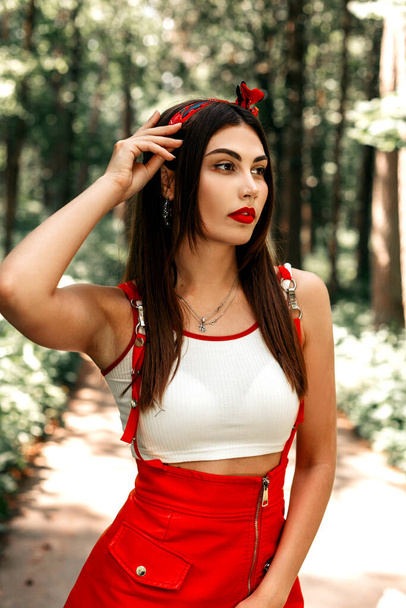 Frisches Porträt einer Modefrau mit rotem Lippenstift und sexy Lippen in einem schönen stylischen Kleid mit rotem Kopftuch an einem Sommertag im Wald. - Foto, Bild
