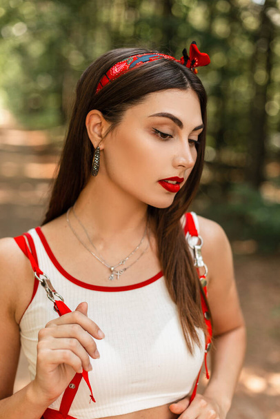 Καλοκαίρι πορτρέτο της όμορφης νεαρής γυναίκας με κόκκινο κραγιόν και σέξι χείλη σε λευκό νεανικό τοπ με μοντέρνα μπαντάνα βόλτα στη φύση. - Φωτογραφία, εικόνα