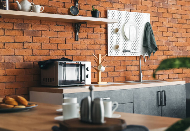Interior of modern kitchen with counters and hanging pegboard on brick wall - Zdjęcie, obraz
