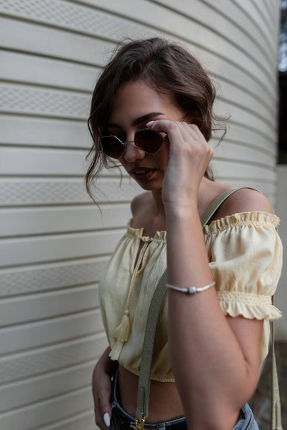 Mooie jonge hipster vrouw model met krullend haar zet op mode zonnebril en wandelingen op straat - Foto, afbeelding
