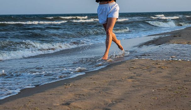 Woman is running ahead on beach of sea. Legs close-up. - Φωτογραφία, εικόνα