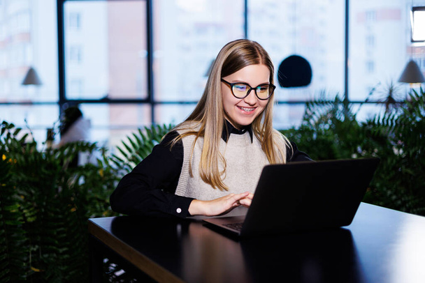 Beautiful smart attractive elegant woman businesswoman in a large company holds an online meeting with international business partners, she sits at a table at the workplace with a laptop - Foto, Imagen