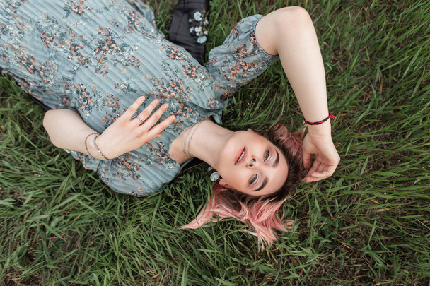 Portrait gorgeous lovely young woman with clean skin with beautiful blue eyes with pink hair in youth flower blue fashionable dress on green grass. Pretty fashion girl rest on nature, Top view - Foto, Imagem