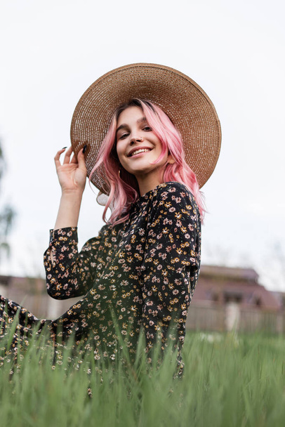 Beauty portrait attractive smiling young woman with pink hair with beautiful eyes in fashionable black dress in straw vintage stylish hat outdoors on nature. Cute positive girl model with sweet smile. - Foto, immagini