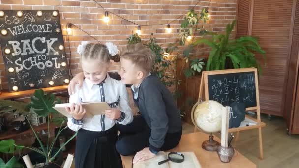 Schoolkinderen - een jongen en een meisje lezen een boek in een omhelzing, fluisteren in hun oren en lachen in de klas tegen de achtergrond van de inscriptie - Welkom! Terug naar school! - Video