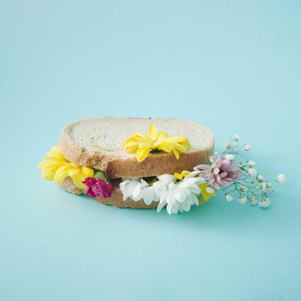 Εαρινό σπιτικό σάντουιτς με πολύχρωμα λουλούδια σε παστέλ μπλε φόντο. Δημιουργική ανθοφορία τροφίμων έννοια. Πλευρική άποψη. - Φωτογραφία, εικόνα