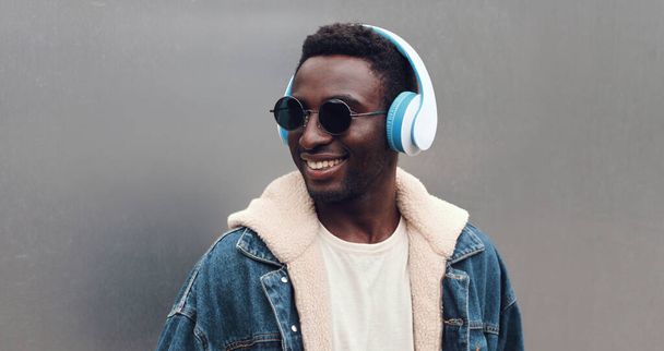 Portrait close up of happy smiling african man in wireless headphones listening to music in a city - Photo, Image